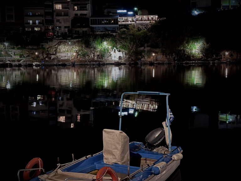 lake of agios nikolaos in the evening with the lights to reflect an water and a small boat is seen in front